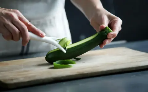 Manos pelando un calabacín para preparar deliciosas recetas con calabacín.