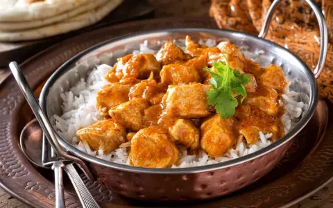 Un delicioso pollo al curry, un plato que evoca los sabores de la India, servido sobre arroz blanco en un cuenco de cobre.