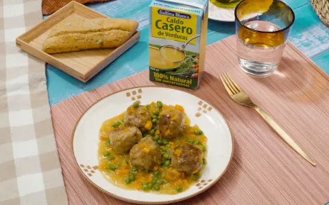 Albondigas a la jardinera en salsa con guisantes y zanahoria, acompañadas de pan y caldo de verduras.