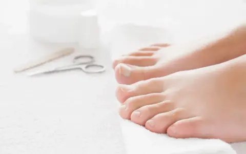 Pies cuidados y herramientas para pedicura sobre toalla blanca.