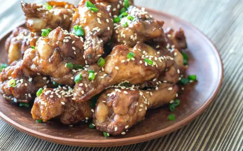 Alitas de pollo glaseadas con sésamo y cebolleta en un plato marrón.