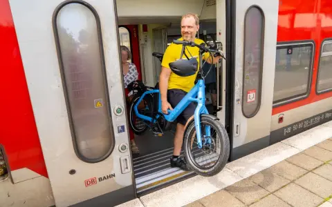 Mann mit blauem E-Bike steigt in den Zug. Perfekt, um das E-Bike im Zug mitzunehmen und die Reise fortzusetzen.