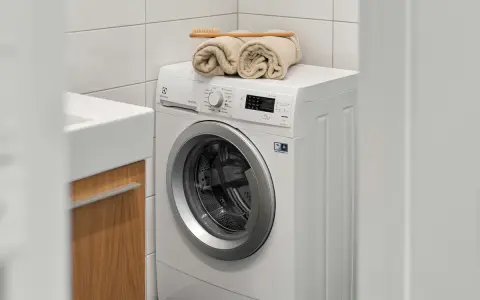 Lavatrice bianca con due asciugamani arrotolati e una spazzola in legno in cima. Ideale per il lavaggio misto in lavatrice.