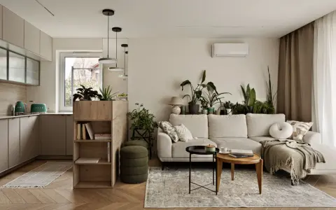 Minimalistyczne wnętrza z dużą ilością zieleni. Jasna kanapa, drewniane meble i kuchnia w neutralnych kolorach tworzą przytulną atmosferę.