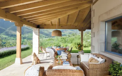 Ideas para como decorar porche de entrada: muebles de mimbre, mesa de comedor, un perro y vistas espectaculares.