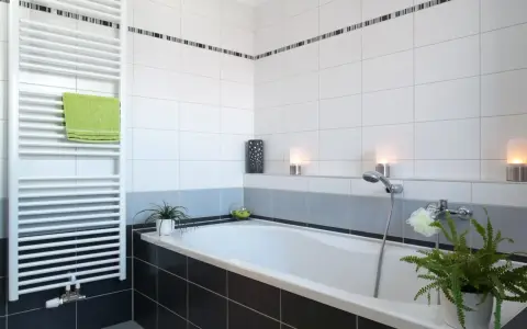 Salle de bain moderne avec baignoire, radiateur blanc et carrelage impeccable. Les joints de carrelage sont parfaits, donnant une finition propre.