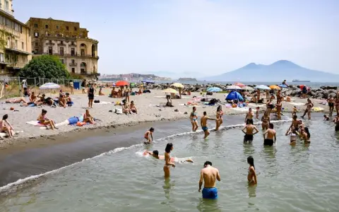 Gente che si gode il sole e il mare sulle spiagge libere di Napoli, con il Vesuvio sullo sfondo.