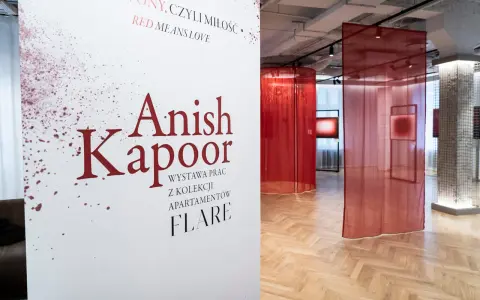Biały plakat z napisem "Anish Kapoor" i czerwonymi rozpryskami na tle wystawy z czerwonymi zasłonami.