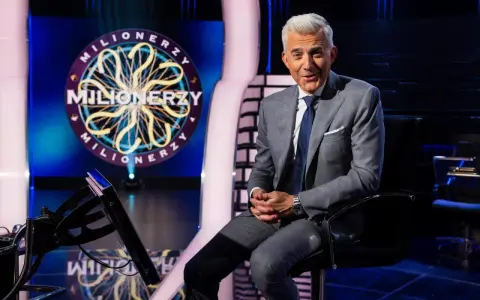 Hubert Urbański w garniturze siedzi na tle logo "Milionerzy". Zastanawia się, ile waży koszyk z pytaniami.