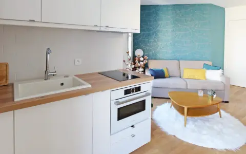 Aménagement petite cuisine moderne avec évier, plaque induction, four et salon cosy avec canapé bleu et jaune.