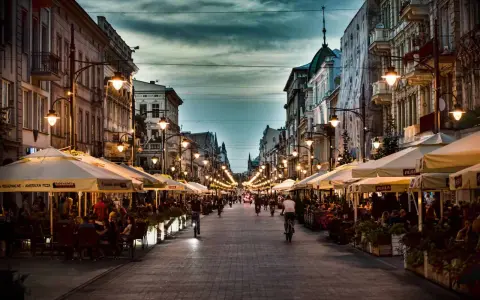Wieczorny spacer po deptaku w mieście w województwie łódzkim nad Wartą. Ludzie siedzą w ogródkach kawiarnianych, rowerzyści przemierzają ulicę.