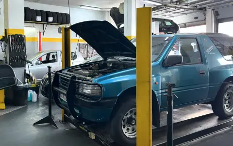 Taller mecánico con coches en reparación. Un todoterreno azul tiene el capó abierto, y se pregunta qué significa elevalunas.