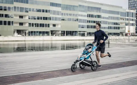 Ein Mann joggt mit Kinderwagen an einer modernen Fassade entlang. Das Kind schläft friedlich im Wagen.