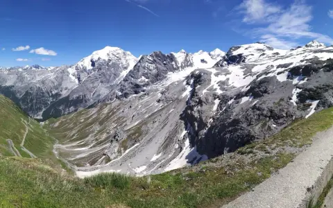 Panoramica mozzafiato dei fotografi sui tornanti dello Stelvio, con vette innevate e un cielo azzurro intenso.