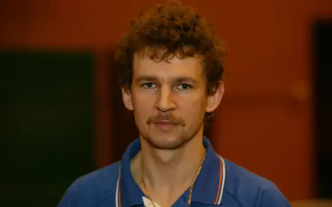 Tomasz Wronka, z kręconymi włosami i wąsami, w niebieskiej koszulce polo.