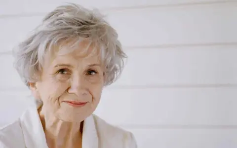 Ritratto di Alice Munro, con capelli grigi spettinati e un sorriso gentile.
