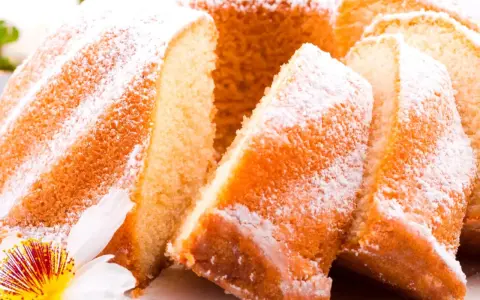 Szybka babka wilgotna, oprószona cukrem pudrem, z widocznymi kawałkami ciasta i ozdobiona kwiatem.