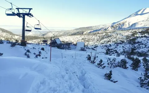Zimowy krajobraz na Kasprowym Wierchu. Kolejka linowa wjeżdża na ośnieżony szczyt, a pod nią rozciąga się dolina pokryta śniegiem.