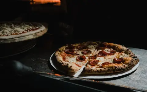 Upieczona pizza pepperoni na talerzu, obok surowa pizza w piecu.