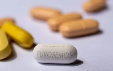 Biała tabletka z napisem FUROSEMIDE na pierwszym planie, otoczona innymi tabletkami w kolorze żółtym i beżowym.