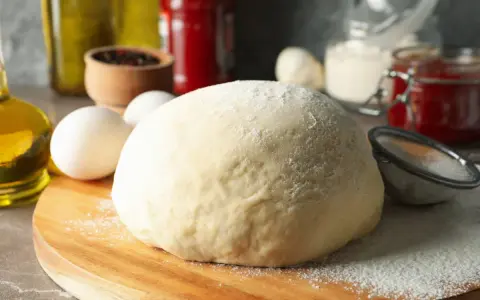 Frischer, fluffiger Teig für schnellen Pizzagenuss liegt bereit. Zutaten wie Eier, Öl und Gewürze deuten auf eine köstliche Pizza hin.