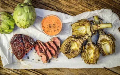 Saftiges Steak und gegrillte Artischocken mit Dip auf Holzuntergrund.
