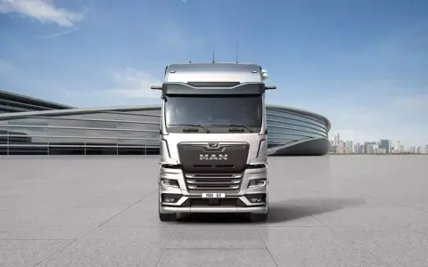 Nowy MAN TGX, lśniący srebrny, przed nowoczesnym budynkiem.