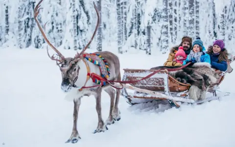 Familie im Rentierschlitten im verschneiten Wald, ein magischer Ausflug im Weihnachtsmann-Dorf Finnland.