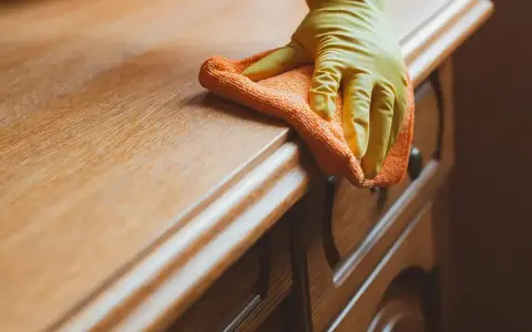 Rękawiczka i ściereczka czyszczą drewnianą szafkę. Dowiedz się, czym zmyć klej z szafki, by przywrócić jej dawny blask.