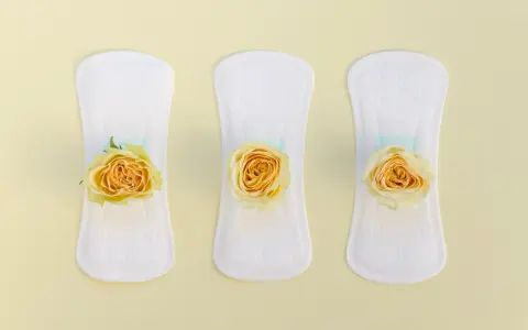Tres compresas blancas con rosas amarillas, simbolizando un flujo amarillo antes de la regla.