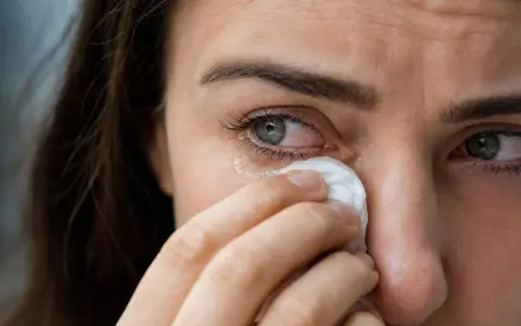 Occhi lacrimosi: una donna si asciuga le lacrime con un fazzoletto. Le cause possono essere molteplici, dal dolore alla stanchezza.