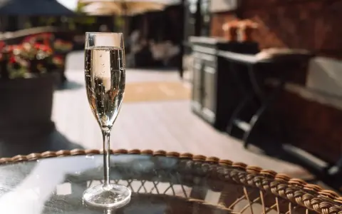 Ein Glas Sekt auf einem Tisch im Freien. Auch wenn Sekt kein Verfallsdatum hat, sollte er frisch genossen werden.
