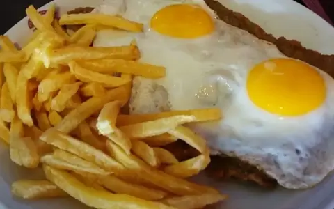 Un plato de milanesa a caballo argentina con papas fritas doradas y dos huevos fritos con yemas perfectas.