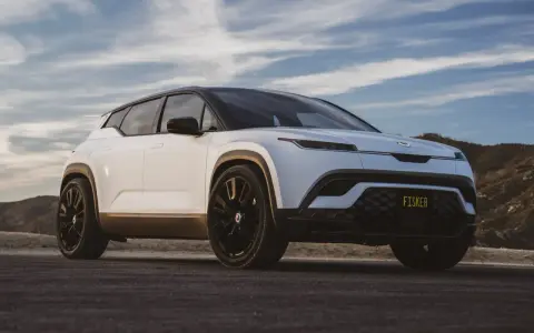 Biały SUV Fisker z czarnym dachem i przyciemnianymi szybami, zaparkowany na drodze z widokiem na wzgórza i niebo.