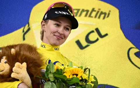Kasia Niewiadoma strahlt im gelben Trikot, hält einen Löwen-Plüschtier und Blumen.