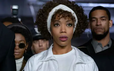 Naomi Ackie como Whitney Houston, lista para cantar "I Wanna Dance with Somebody" rodeada de fans y seguridad.