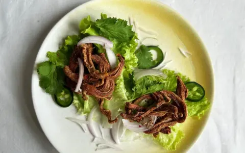 Crujiente oreja de cerdo frita servida sobre lechuga con cebolla morada, cilantro y jalapeño.