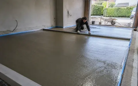 Pracownik wyrównuje świeżą wylewkę betonową na zewnątrz, przygotowując podjazd.