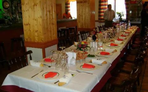 Mesa larga y elegante lista para comer en Riopar, con copas, platos y panecillos.