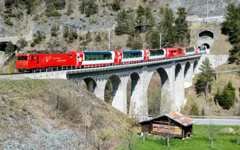 The red and white Glacier Express train travels across a stone viaduct, a scenic journey from Chur to Zermatt.