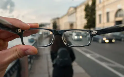 Okulary trzymane przed zamazanym miejskim tłem z samochodami.