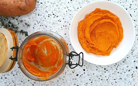 Pomarańczowe purée z batatów w słoiku i na talerzu, obok surowy batat i gałązka tymianku.