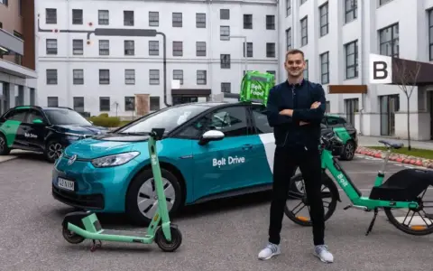 Ein Mann steht stolz neben einem Bolt Drive Auto, E-Scooter und Fahrrad. Er ist ein Bolt Fahrer, der umweltfreundliche Mobilität fördert.