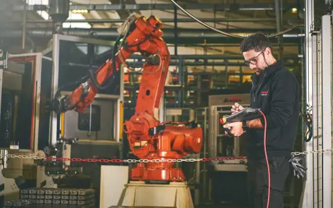 Un tecnico controlla un braccio robotico rosso in una fabbrica, dimostrando la meccatronica cos'è: l'integrazione di meccanica, elettronica e informatica.
