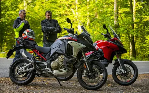 Dwóch motocyklistów przy dwóch motocyklach Ducati Multistrada V2, jeden szary, drugi czerwony, na tle leśnej drogi.