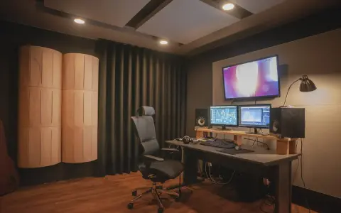 Studio nagraniowe z monitorem studyjnym, dwoma ekranami, wygodnym fotelem i panelami akustycznymi, które pomagają w kontroli **damping factor**.