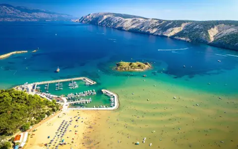 Piaszczyste plaże w Chorwacji, z turkusową wodą, łodziami w marinie i ludźmi cieszącymi się słońcem.