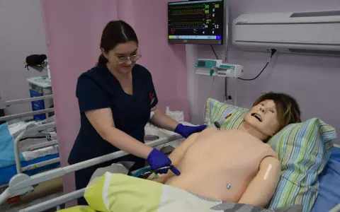 Studentka medycyny ćwiczy na fantomie, jak wyglądają studia medyczne. Monitor pokazuje parametry życiowe.