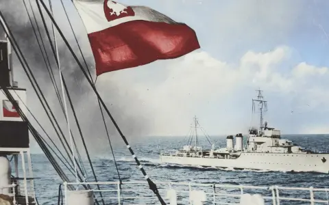 ORP Wicher płynie po wzburzonym morzu. Na pierwszym planie widać fragment statku i polską flagę.