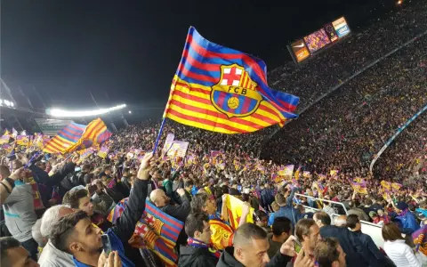 Tłum kibiców na stadionie unosi flagi z herbem FC Barcelona. Flaga Katalonii powiewa dumnie nad głowami fanów.